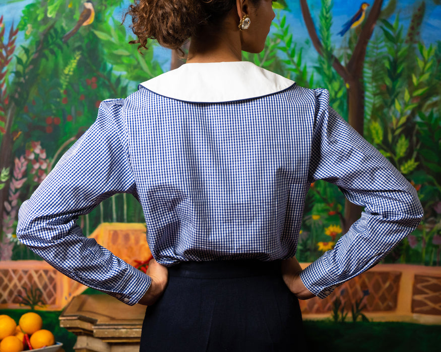 Navy gingham shirt, long sleeve, puff shoulder, white collar with navy outer piping, bee embroidery on each side of collar.  Edit alt text